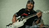 a man playing a white guitar with a bandana on his head