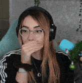 a woman wearing headphones and a necklace with a heart on it covering her mouth