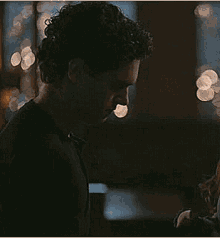 a man with curly hair is standing in a dark room looking at a book .