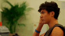 a young man with curly hair is sitting in front of a palm tree .