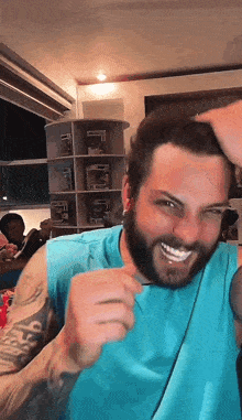 a man with a beard wearing a blue tank top is smiling with his hand on his head