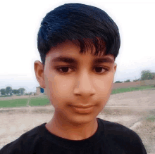 a young boy in a black shirt looks at the camera with a field in the background