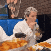 a man is sitting at a table eating food and drinking a glass of orange juice