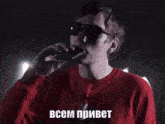 a man wearing sunglasses and a red shirt is singing into a microphone in russian .