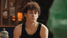 a young man with curly hair is wearing a black tank top