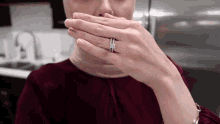 a woman is covering her mouth with her hands while wearing a wedding ring