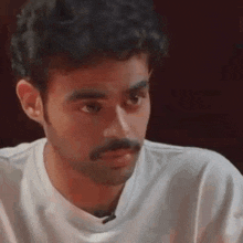 a close up of a man with a mustache wearing a white t-shirt .