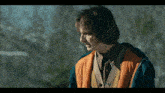 a man wearing an orange vest and a blue jacket looks to the side