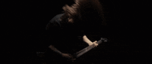 a man is playing a guitar in a dark room with his hair blowing in the wind .