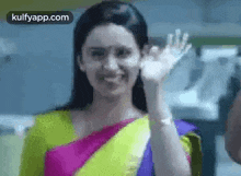 a woman in a colorful saree is waving her hand in a kitchen .