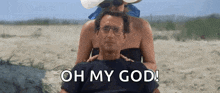 a man is sitting on a beach with a woman behind him and the words `` oh my god '' written on the screen .