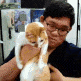 a man wearing glasses holds a cat in his arms