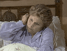 an elderly woman in a purple shirt is laying in bed
