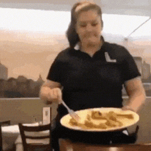 a woman in a black shirt is sitting at a table with a plate of food .