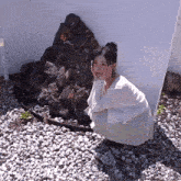 a woman in a white dress is kneeling down in front of a rock wall