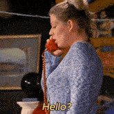 a woman in a blue sweater is talking on a red telephone with the words hello written on it