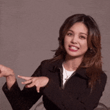 a woman in a black jacket is making a gesture with her hands while wearing a white shirt .