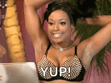 a woman in a bra is sitting in front of a laptop and smiling .
