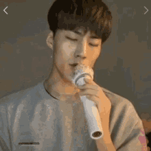 a young man is singing into a microphone while wearing a gray shirt .