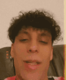 a young man with curly hair is sitting on a couch with his eyes closed and his mouth open .