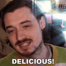 a man with a beard and mustache is smiling with the words delicious below him