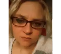 a woman wearing glasses and a sweater is making a funny face
