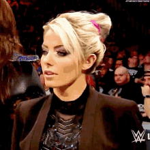 a woman with blonde hair and a pink headband is standing in front of a crowd with a w logo on her chest .