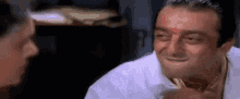 a man with a red dot on his forehead is smiling while talking to another man .