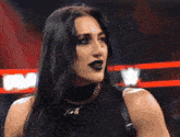 a woman wearing black lipstick and a necklace stands in front of a sign that says wwe