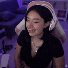 a woman wearing a black shirt and a necklace with a star pendant is smiling in a pink and white chair