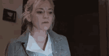 a woman in a denim jacket and white shirt is standing in front of a door .