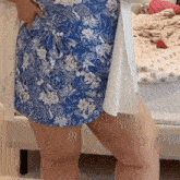 a woman wearing a blue and white floral dress is standing in front of a bed .
