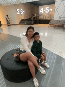 a woman sits on a black ottoman with a little boy in front of a sign that says 2-3 and 4-5