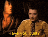 a man in a yellow shirt and tie says have you built in front of a lord of the rings poster