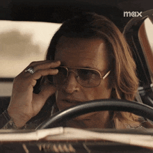 a man wearing sunglasses and a ring is sitting in a car with the word max on the bottom right