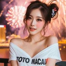 a woman wearing a toto macau shirt stands in front of a fireworks display