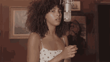 a woman with curly hair is standing in front of a microphone and a painting