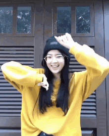 a woman wearing a yellow sweater and a black beanie is smiling