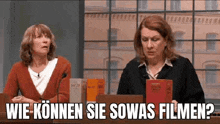 two women are sitting at a table in front of a microphone . one of the women is holding a book .