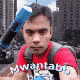 a man wearing a red shirt and a backpack is holding a blue object on his head and the words mwantabb boss are visible