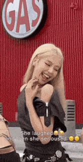 a girl laughing in front of a gas sign