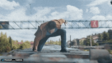 a man in a brown jacket is crawling on a roof with the twitter username pranay_varma below him