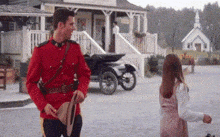 a man in a red uniform is holding a hat and talking to a girl in front of a church .