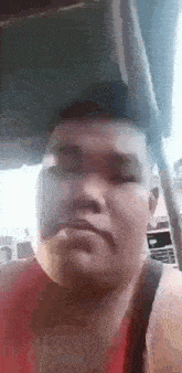 a man in a red tank top is making a funny face while sitting in a car .