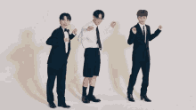 three men in suits and bow ties are dancing in front of a white wall