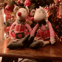 two stuffed mice wearing red and white striped clothes are sitting on a table in front of a christmas tree