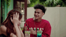 a man and a woman are sitting at a table with a drink in their hand .