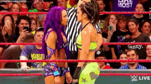 two female wrestlers are facing each other in a wrestling ring while a crowd watches .