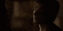 a person is sitting at a table in a dark room with a bottle of alcohol in the background .