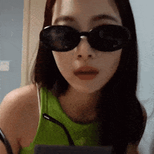 a woman wearing sunglasses and a green tank top looks at the camera